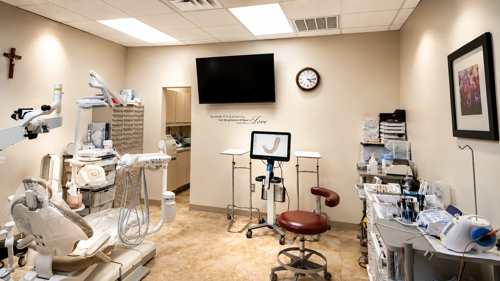 A SoftDental operatory showing the iTero digital scanner with a 3D intraoral scan visible on screen, alongside the Leica microscope, dental chair, scripture wall art, and a crucifix